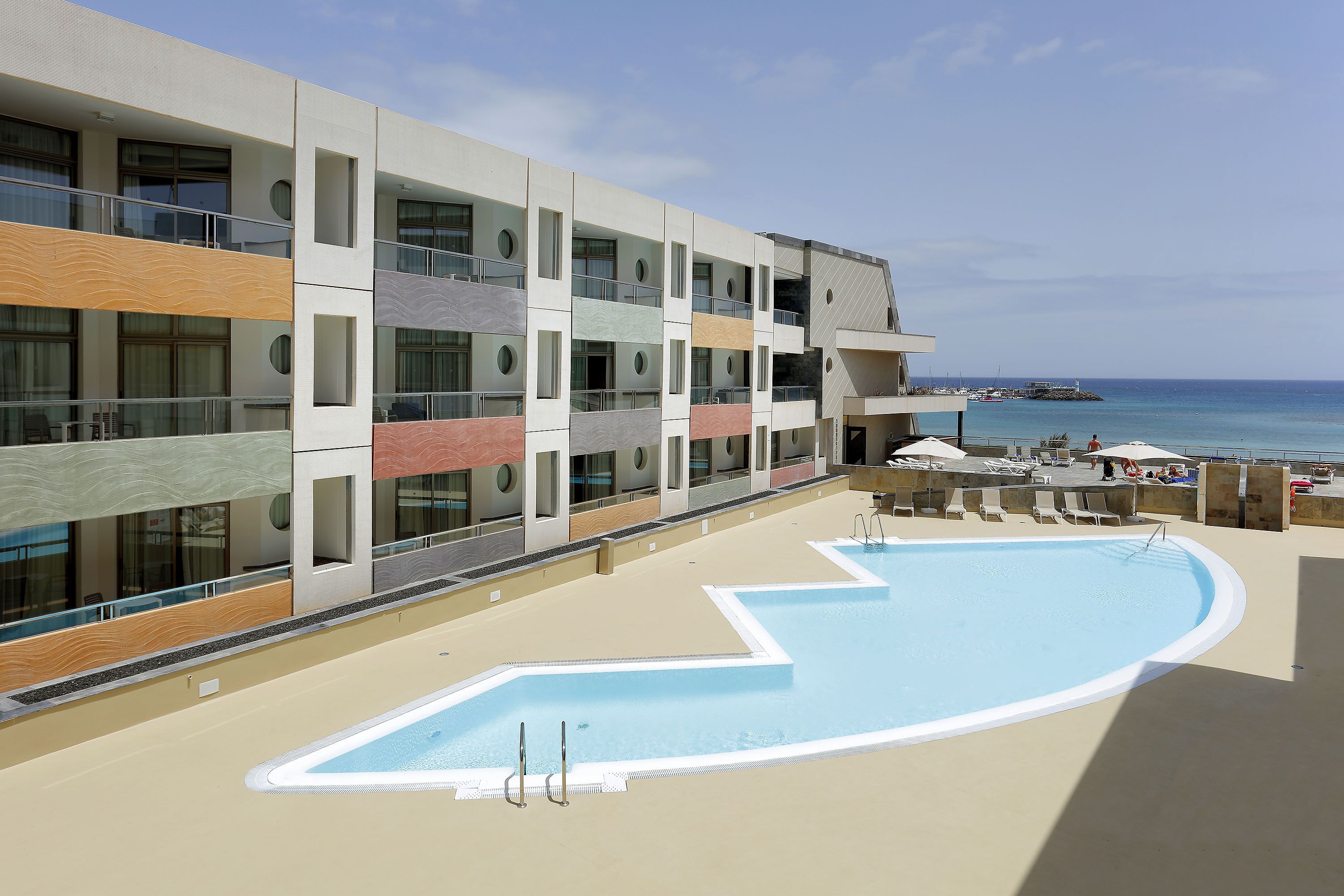 A modern building with a pool area, balconies, and a view of the sea.