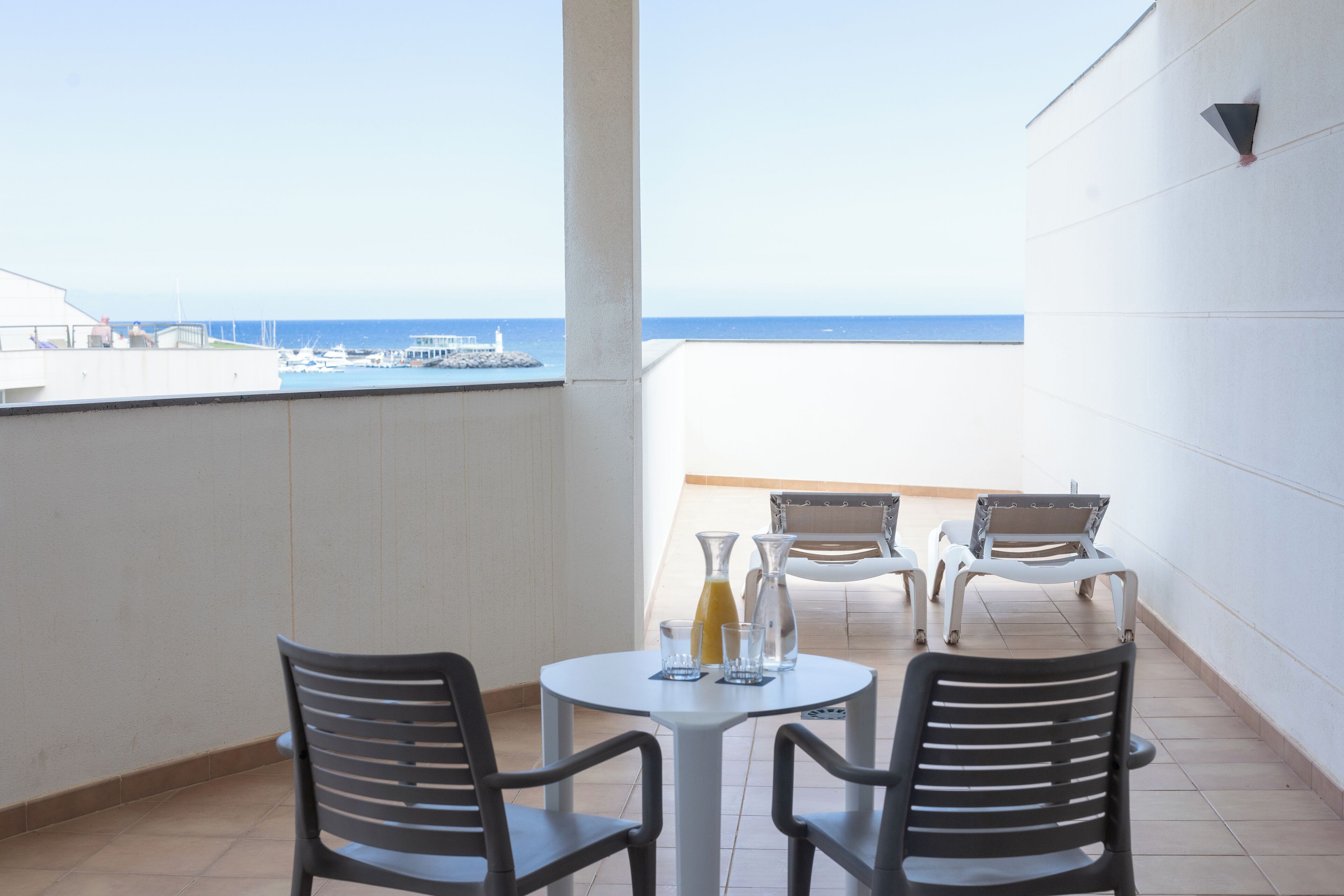 Un balcón con mesa y sillas, vista al mar y un edificio al fondo.