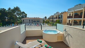 Un balcón con sillones de descanso y un jacuzzi, con vistas a una zona de piscina y edificios.