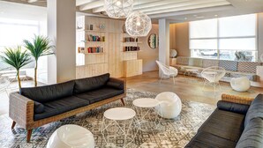 Un salón moderno con un sofá negro, mesas redondas blancas y una lámpara de techo con diseño geométrico.