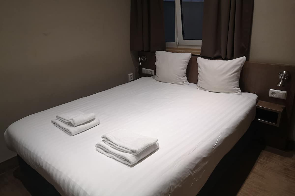 A neatly made bed with white linens and two folded towels.