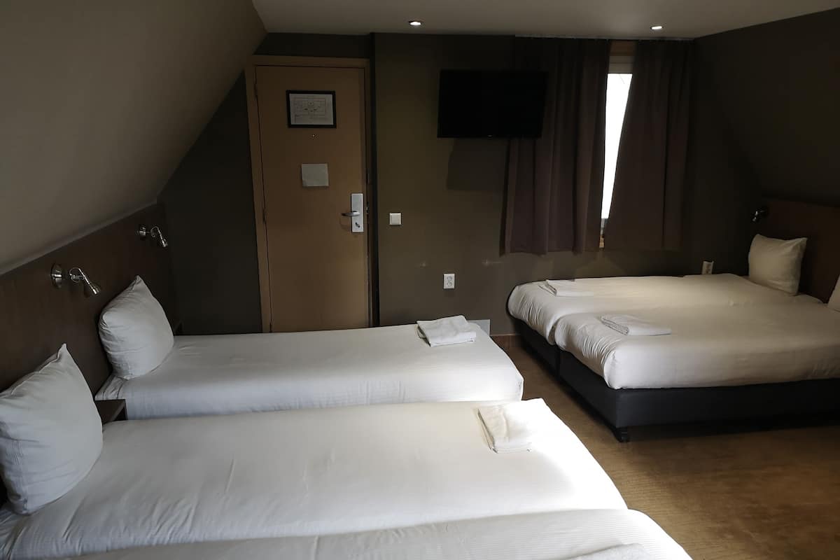 A hotel room with three single beds, a TV mounted on the wall, and a door with a framed diagram.