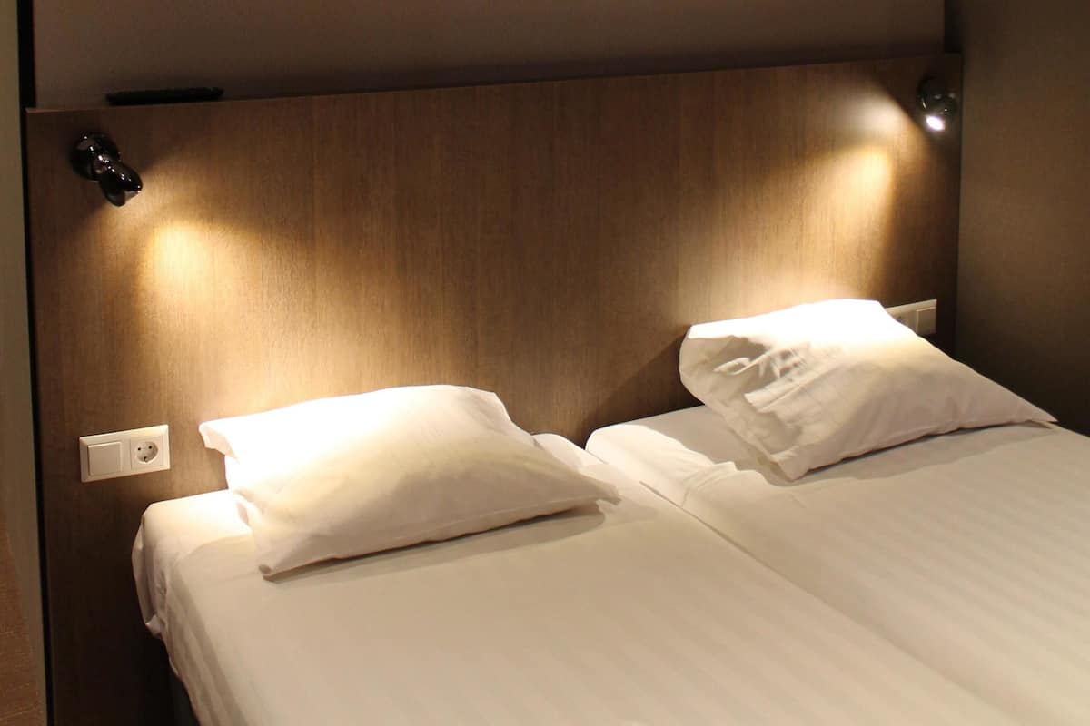 A hotel room with a wooden headboard, two white pillows, and a bedside table with a lamp.