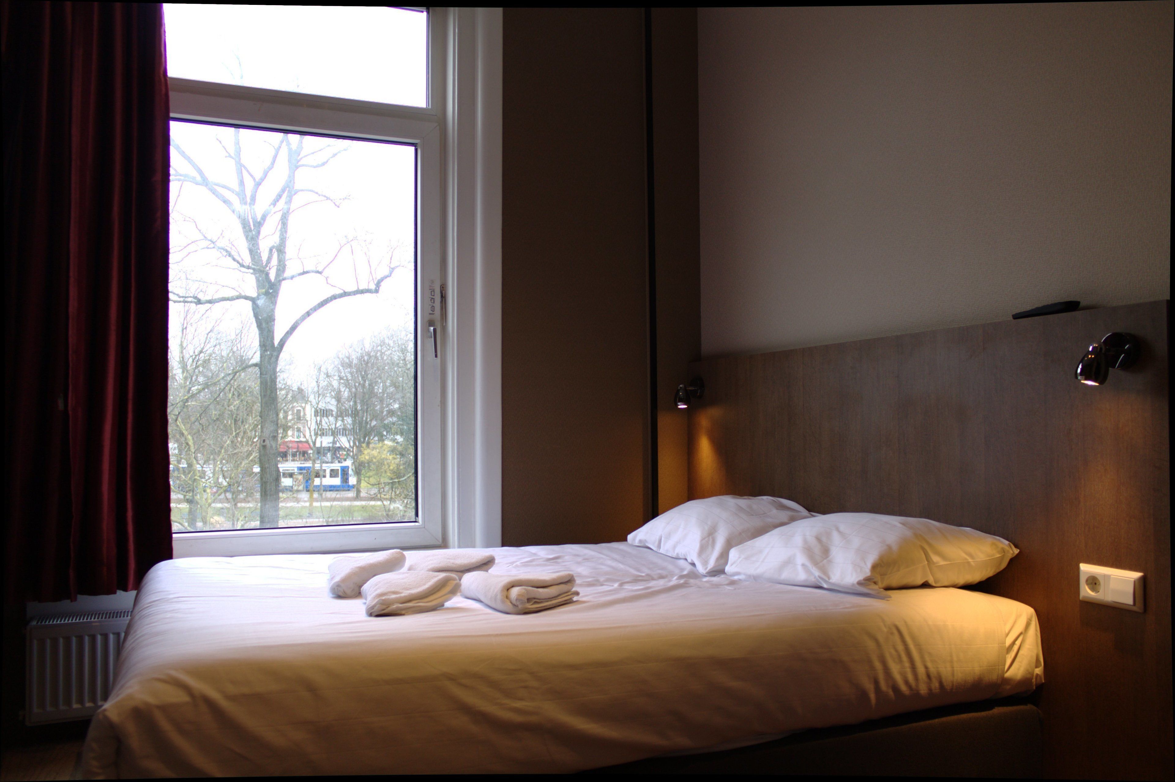 Hotellihuone, jossa on sänky, ikkuna ja näkymä puistoon.