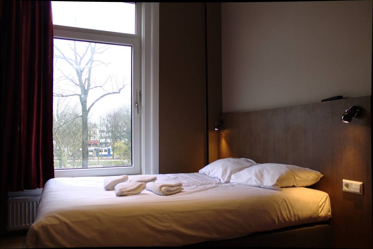 A hotel room with a bed, a window, and a view of trees.