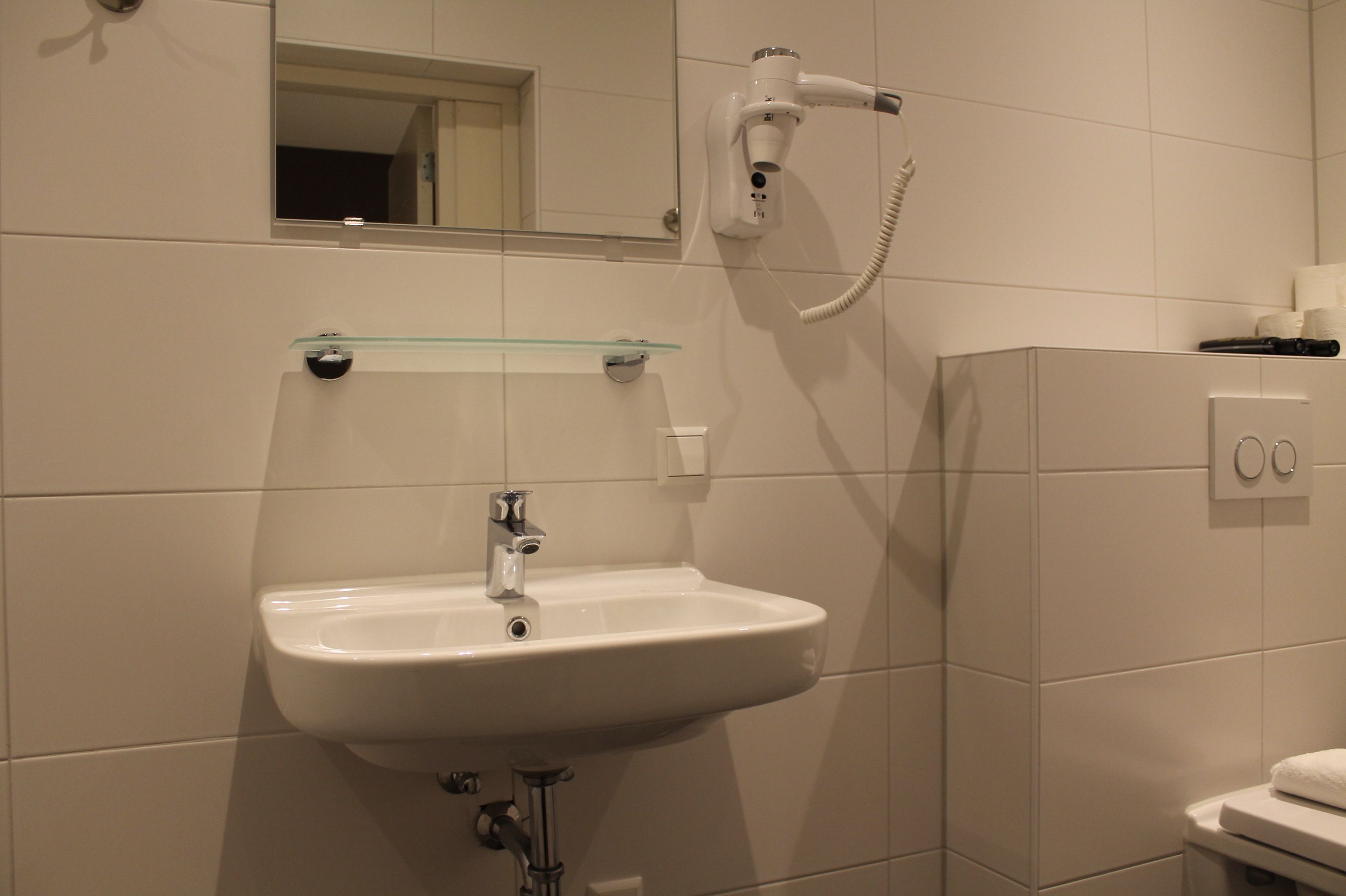 Un baño con un lavabo blanco, un espejo, un secador de pelo y un estante de vidrio.