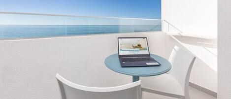 A laptop on a small table with a view of the sea.
