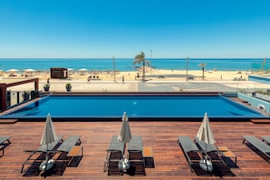 A pool area with lounge chairs and umbrellas, overlooking a beach with umbrellas and a palm tree. - Dom Jose Beach Hotel (Loulé)