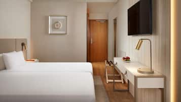 Una habitación de hotel moderna con una cama grande, un escritorio con lámpara, un televisor de pantalla plana y un cuadro en la pared.