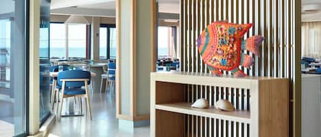 Un hall d’hôtel moderne doté d’une grande paroi vitrée donnant sur l’océan, de meubles en bois et d’une sculpture décorative représentant un poisson.