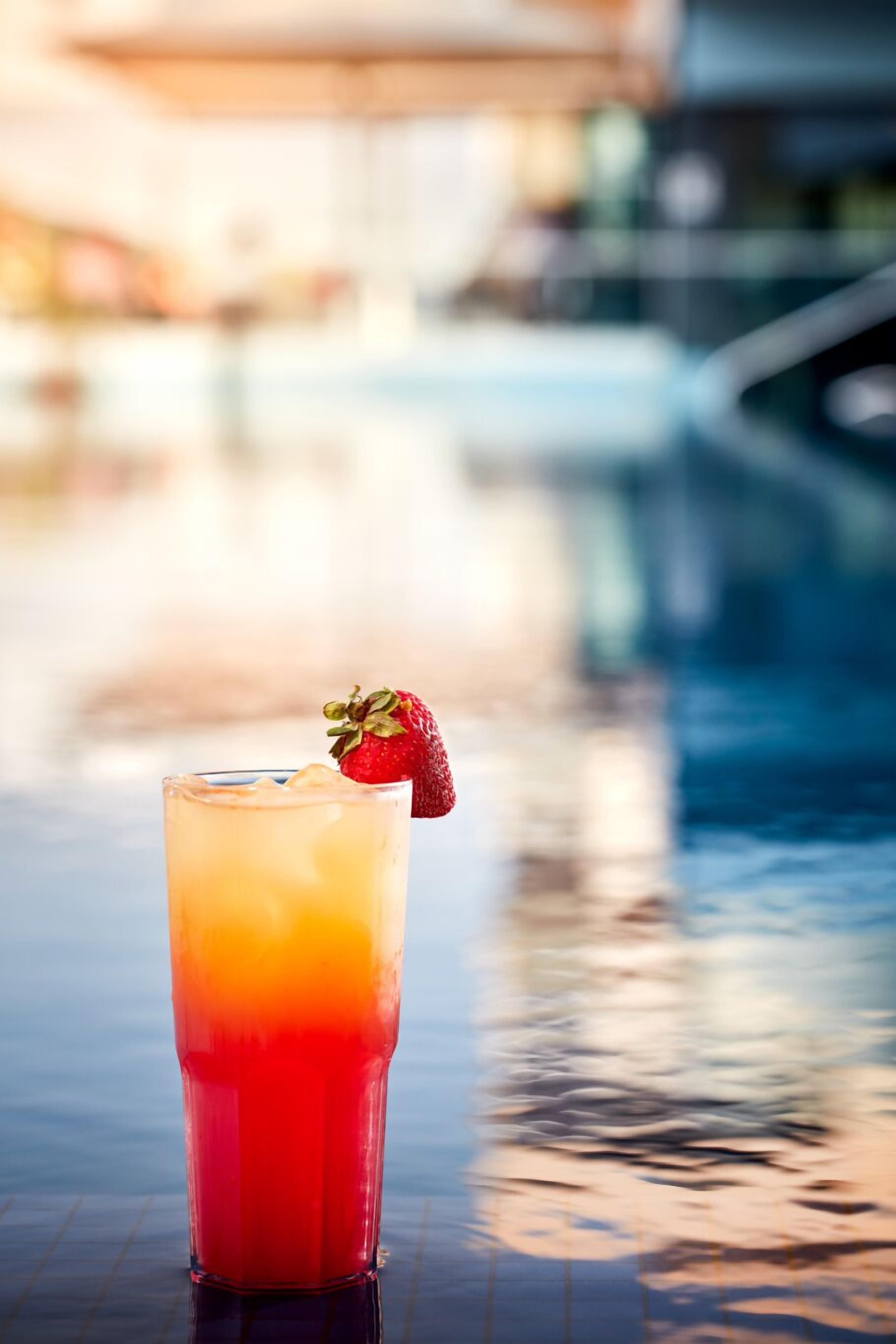 A glass of red drink with a strawberry garnish on a reflective surface.