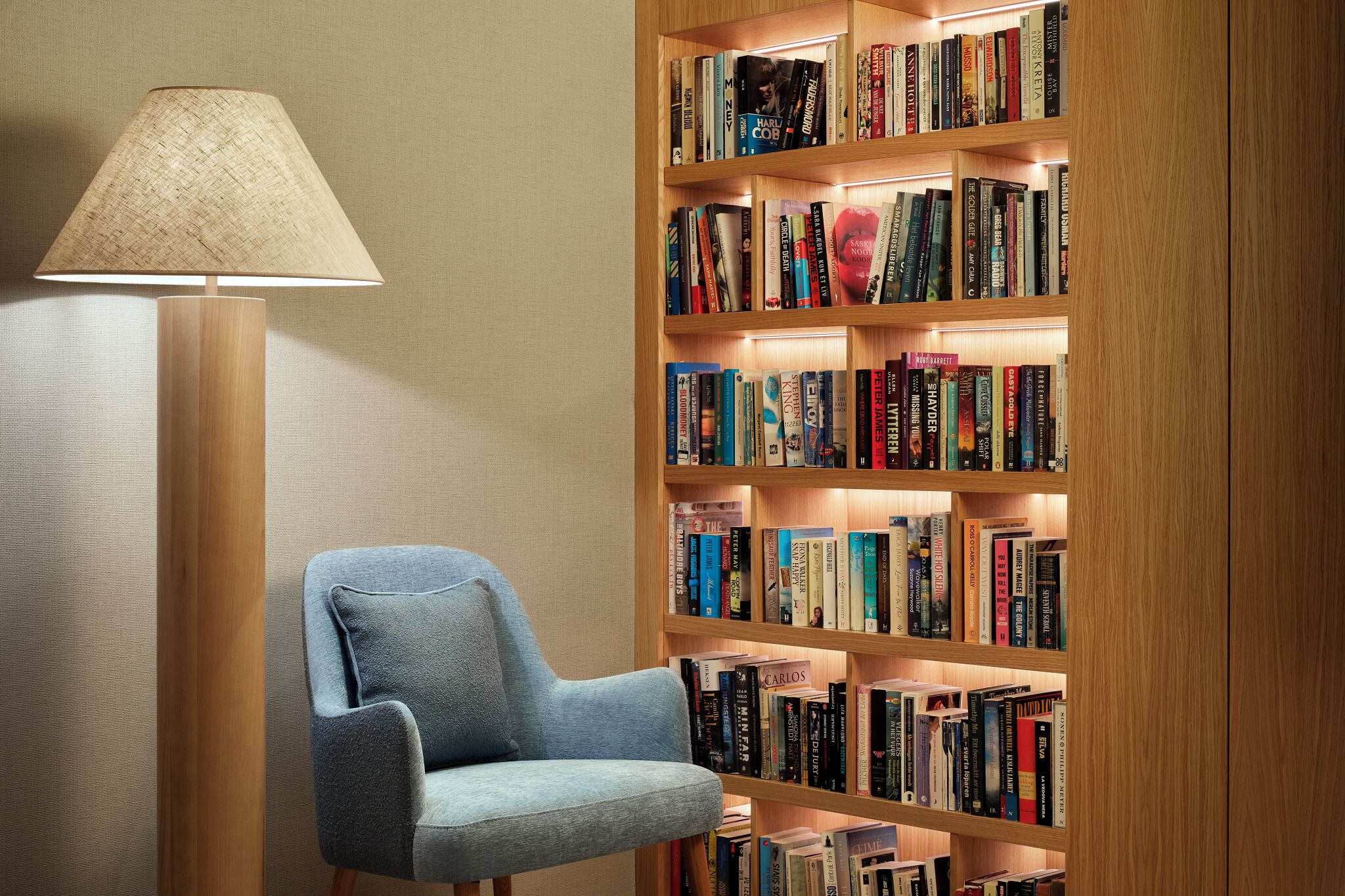 A room with a bookshelf filled with books, a lamp, and a blue armchair.
