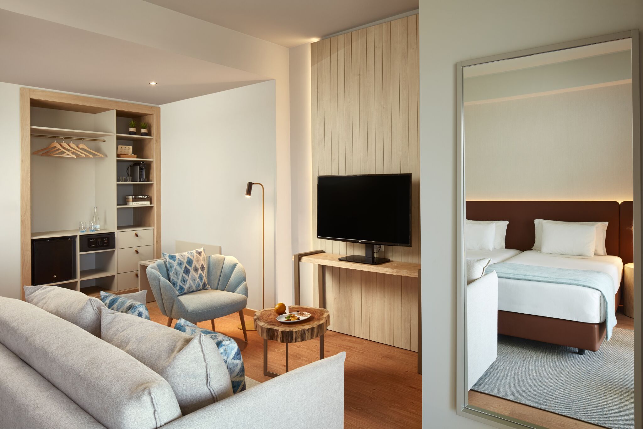 A modern hotel room with a sofa, armchair, bedside table, TV, and a bed.