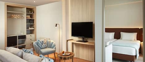 A modern hotel room with a sofa, armchair, bedside table, TV, and a bed.