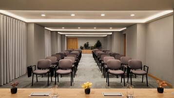 A conference room with rows of chairs, a wooden table at the front, and a carpeted floor.