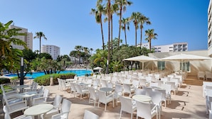 An outdoor patio with white wicker furniture, a pool, palm trees, and a clear blue sky. - Hipotels Said (Sant Llorenc des Cardassar)