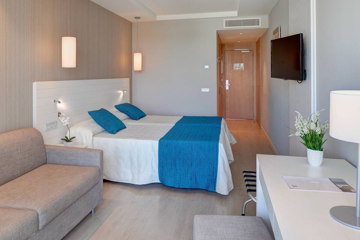A modern hotel room with a bed, a sofa, a desk, and a TV.