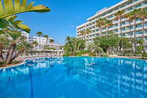 Un hotel con piscina, palmeras y un cielo azul despejado.