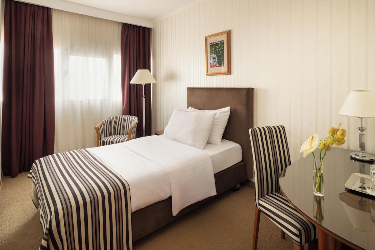 A hotel room with a bed, two chairs, a dining table, a lamp, and a vase with flowers.