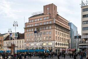 Una plaza urbana concurrida con un edificio destacado que tiene una torre con reloj y un tranvía.
