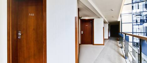 A hotel corridor with wooden doors numbered 502 and 503, a carpeted floor, and a glass railing on the right.