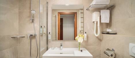 Un baño moderno con ducha, lavamanos, espejo, toallero y dispensador de papel higiénico.