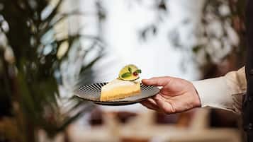 A hand holding a slice of cheesecake with a lime slice on a black and white plate.