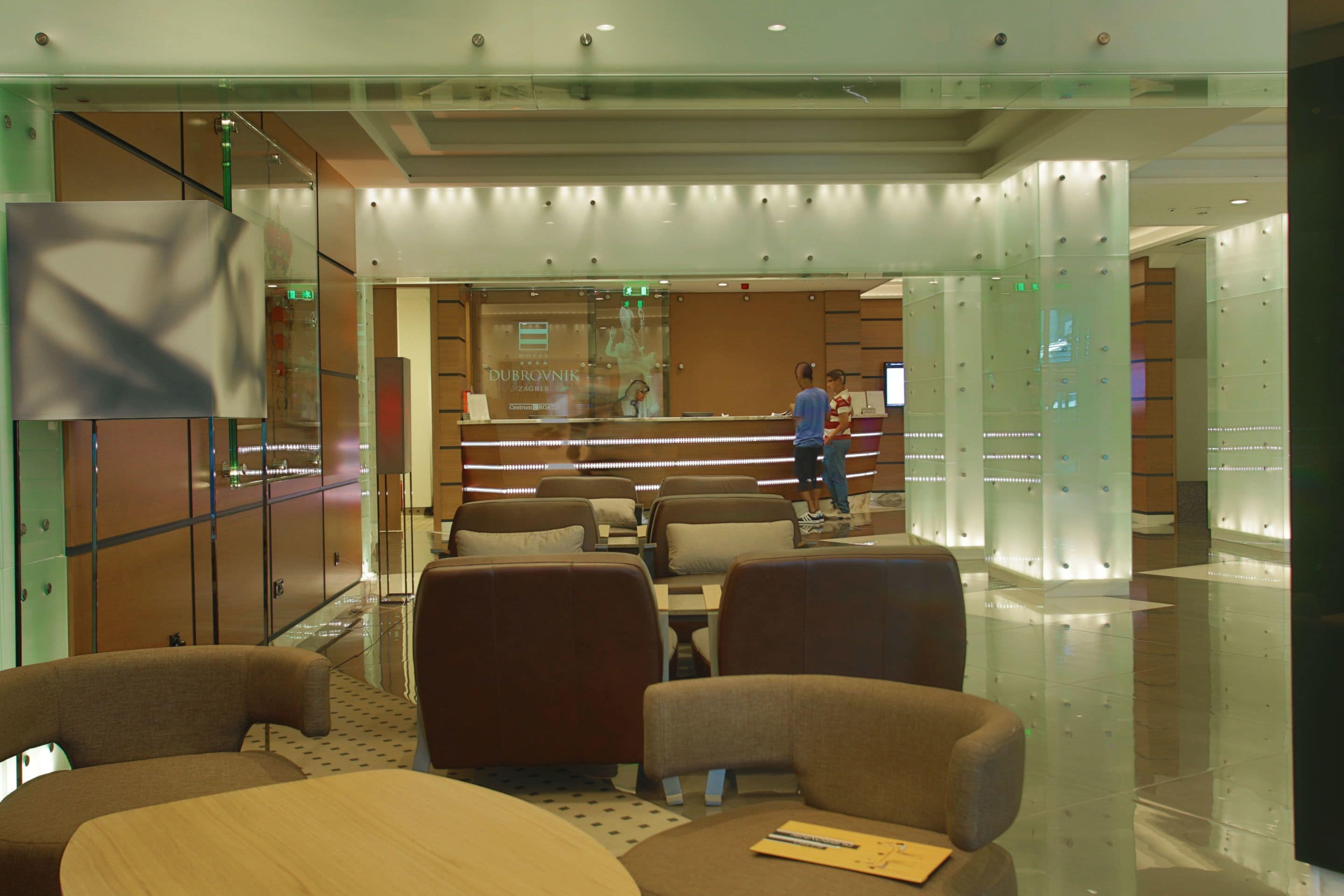 A modern hotel lobby with a reception desk, seating area, and glass partitions.