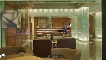 A modern hotel lobby with a reception desk, seating area, and glass partitions.
