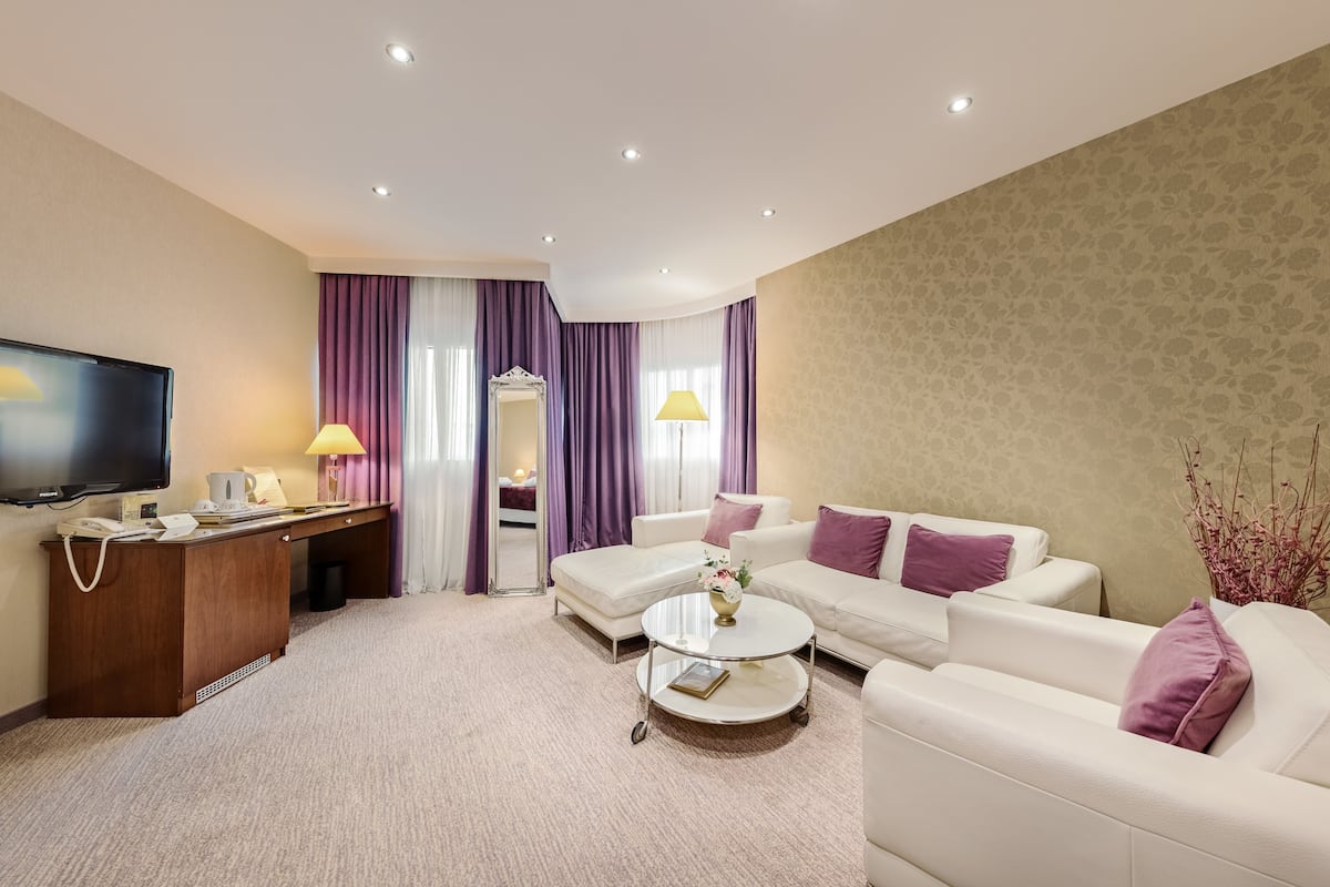 A modern hotel room with a flat-screen TV, a wooden desk, a white sofa, and a round coffee table.