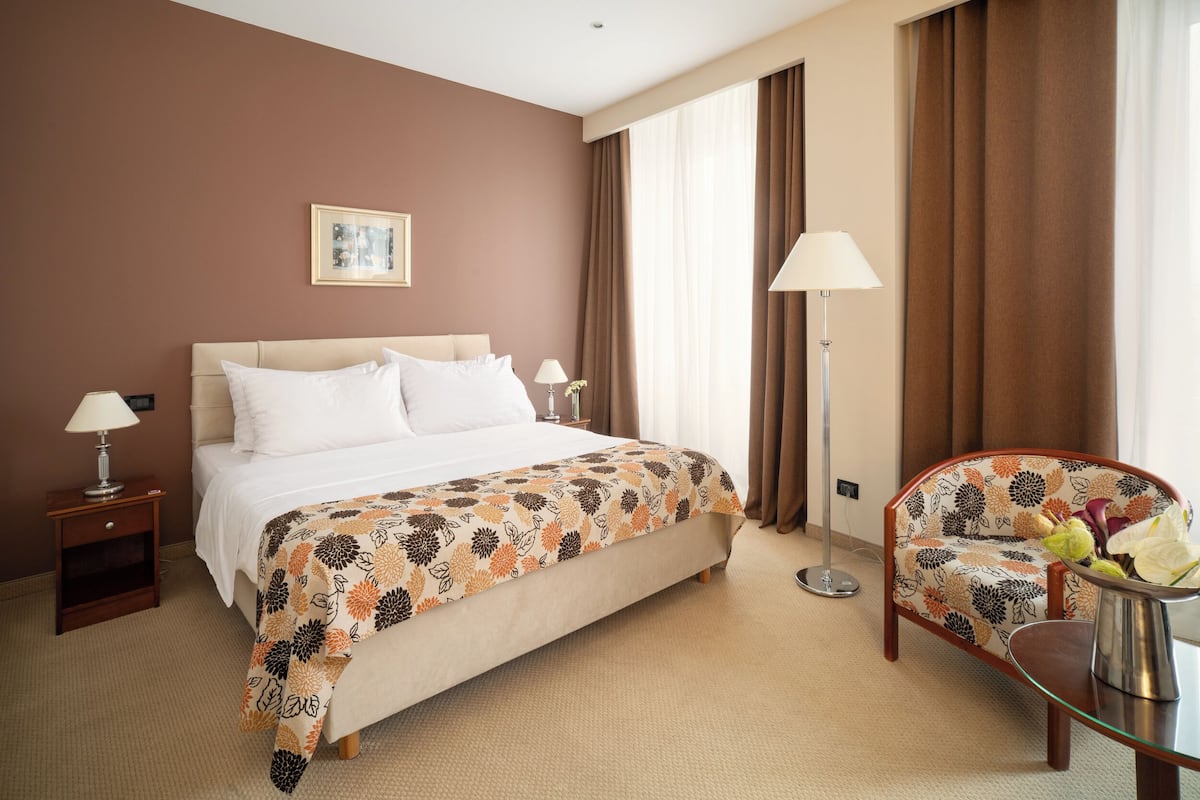 A hotel room with a bed, two bedside tables with lamps, a chair, a floor lamp, and a picture on the wall.