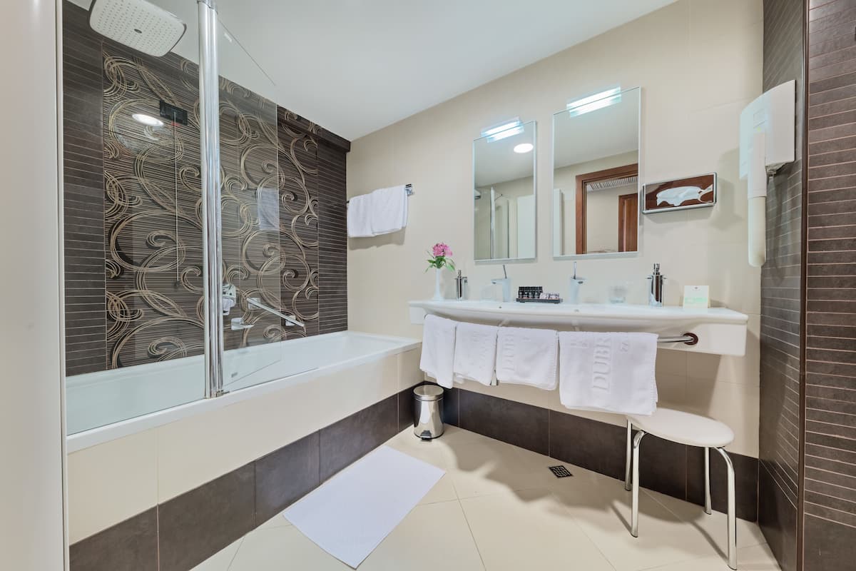 A modern bathroom with a glass-enclosed shower, a large bathtub, and a vanity with a mirror and towel rack.