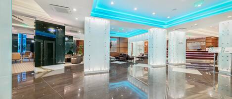 Un vestíbulo de hotel moderno con piso pulido, divisiones de vidrio e iluminación ambiental azul.