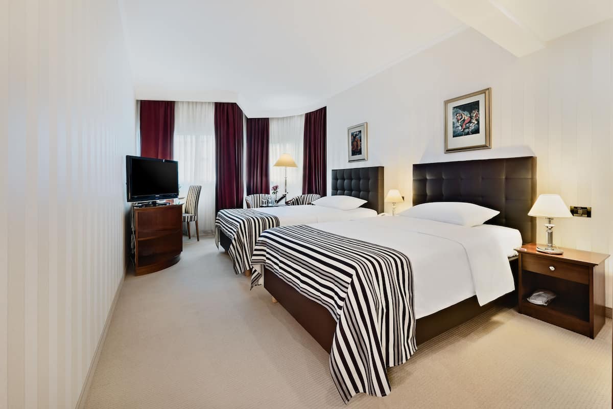 A hotel room with three beds, a TV, a wooden nightstand, and a lamp.