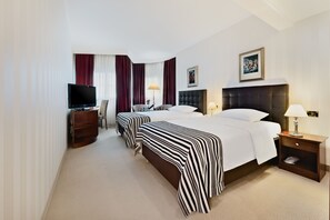 A hotel room with three beds, a TV, a wooden nightstand, and a lamp.