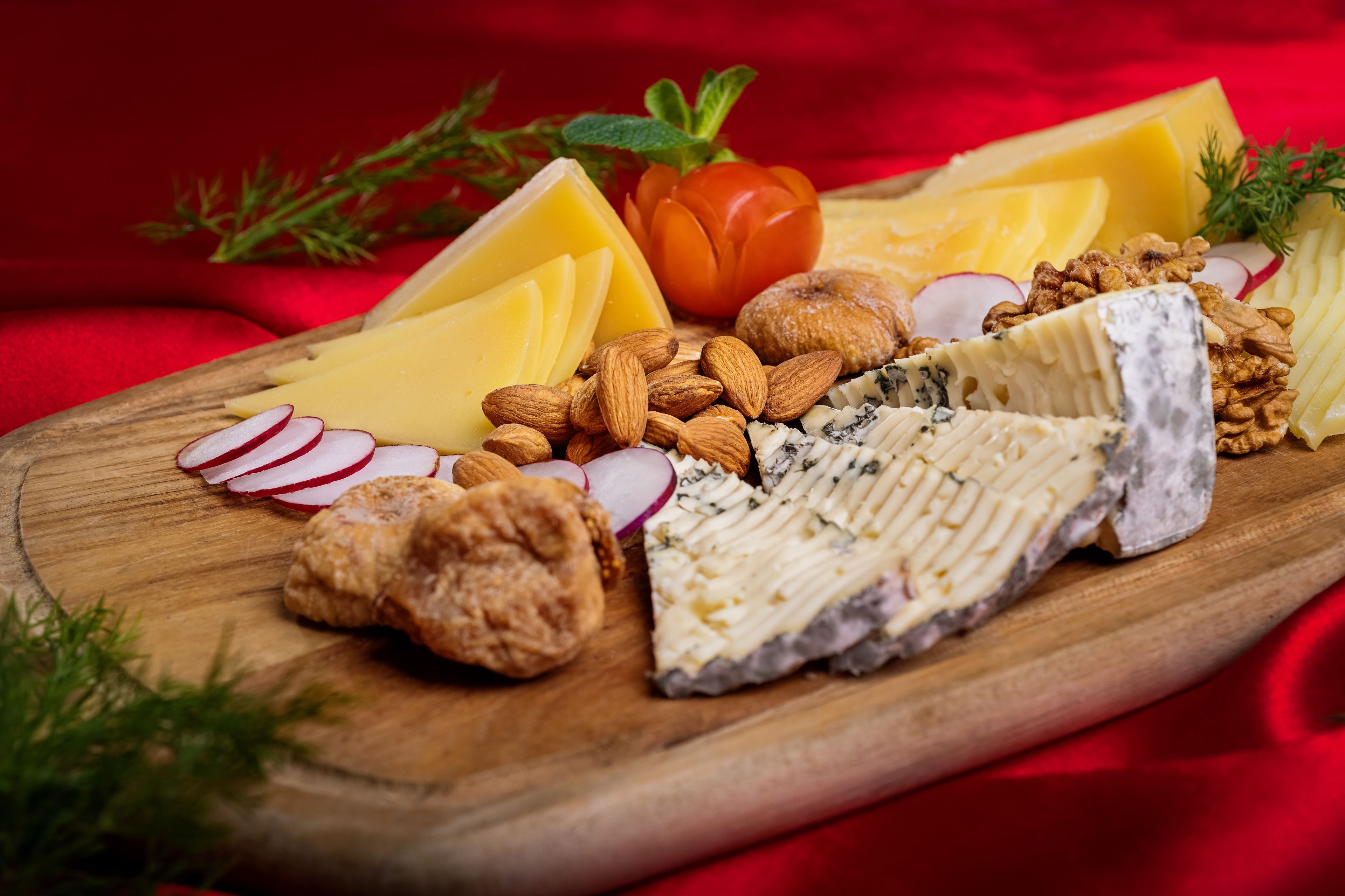 Una tabla de madera con varios quesos, almendras, nueces y rábanos en rodajas.