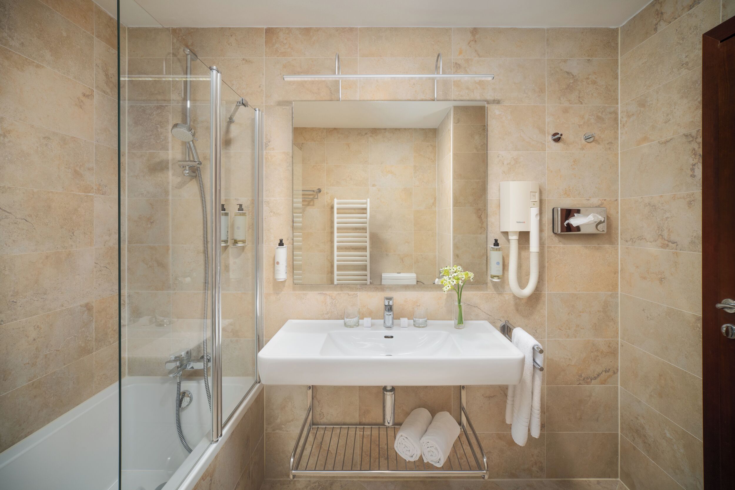 Une salle de bain avec une douche à parois de verre, un lavabo blanc, un porte-serviettes et un miroir.