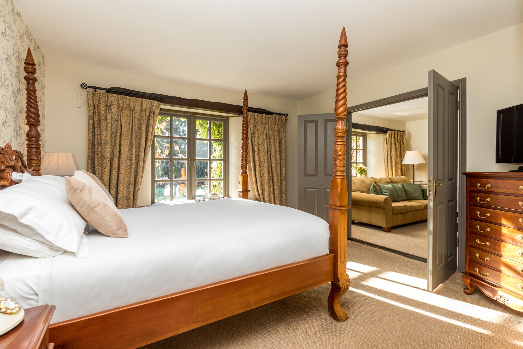 A bedroom with a four-poster bed, a wooden dresser, and a sofa in the adjacent living room.