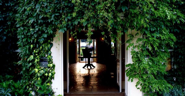 A doorway framed by lush green foliage, leading to an interior space with a wooden floor and a chair. - Brooklodge & Macreddin Village (Macreddin Village)