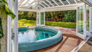 A conservatory with a swimming pool, wooden decking, and outdoor seating. - Brooklodge & Macreddin Village (Macreddin Village)