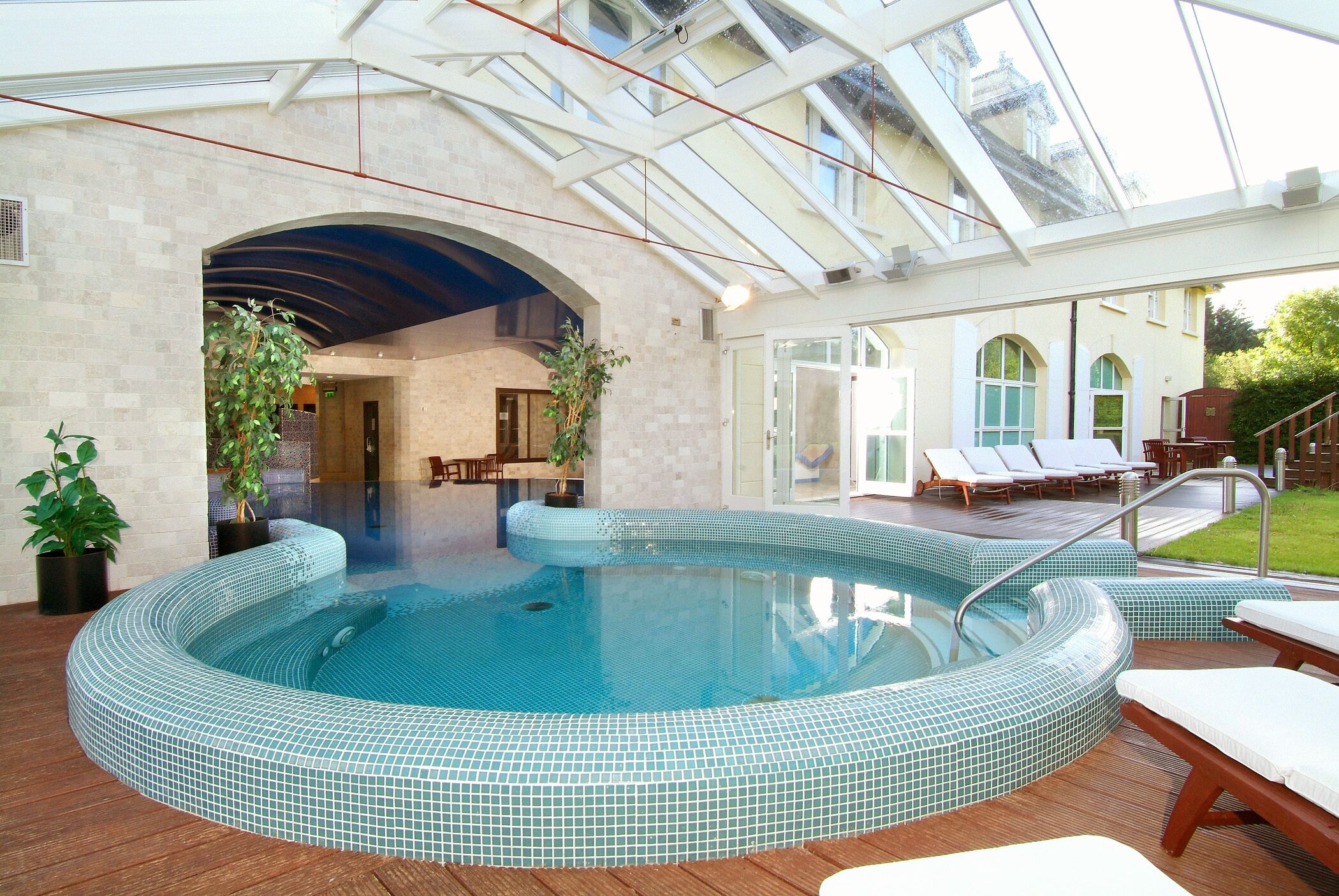 Una piscina con borde de azulejos, rodeada de sillas de descanso y una terraza de madera.
