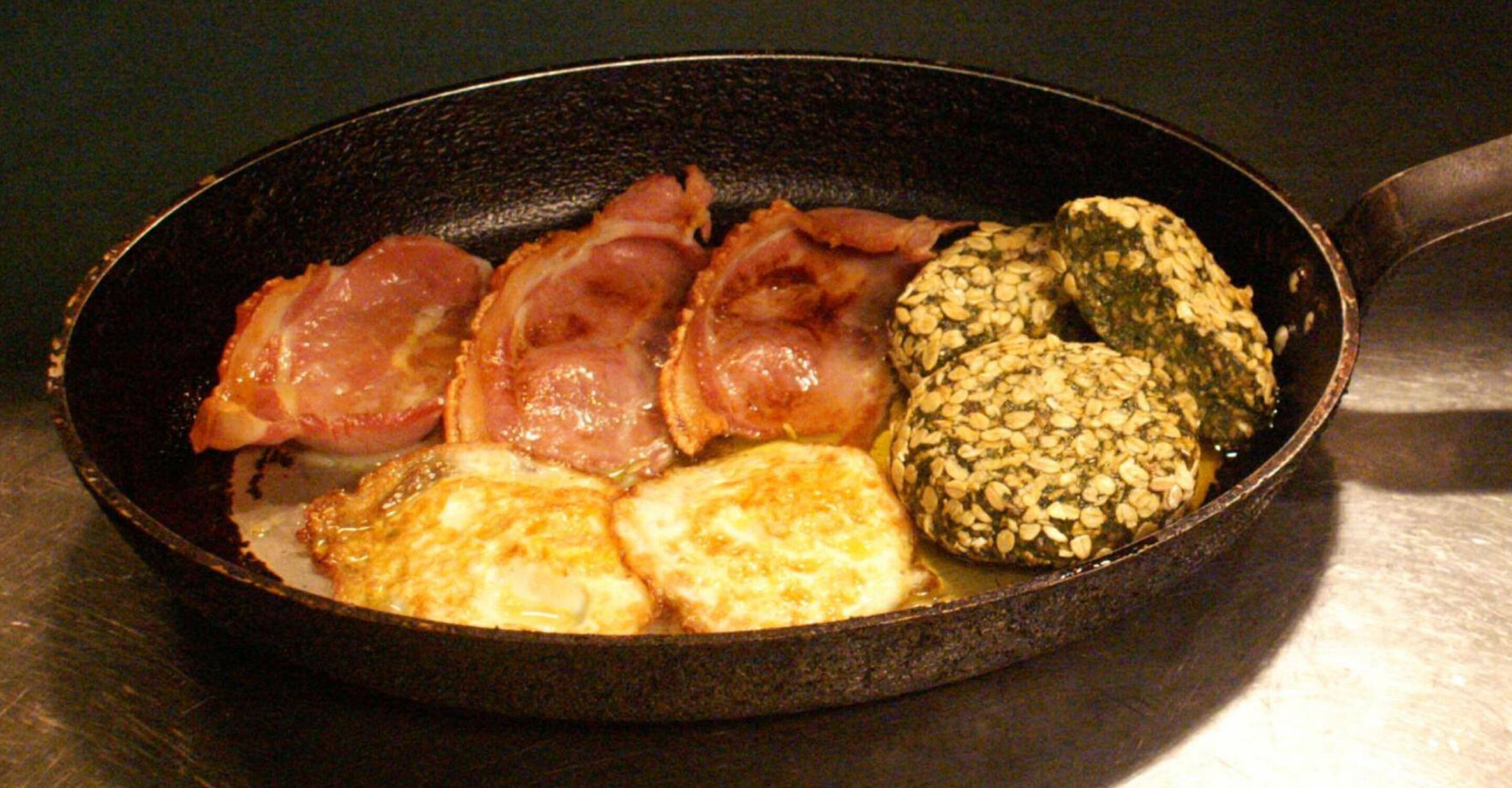A skillet with bacon, eggs, and a rolled item.