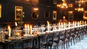 A long dining table set with candles, glasses, and plates, surrounded by chairs in a dimly lit room with chandeliers and framed mirrors on the walls. - Brooklodge & Macreddin Village (Macreddin Village)