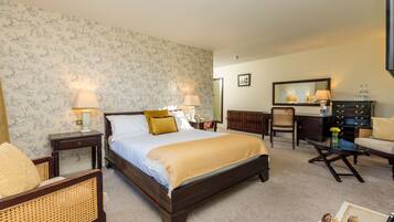 Quarto de hotel com uma cama grande, duas mesas de cabeceira com abajures, uma cômoda de madeira, uma cadeira e uma pequena mesa com um vaso.