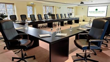 A conference room with a long table, multiple chairs, and a projector screen displaying a logo.