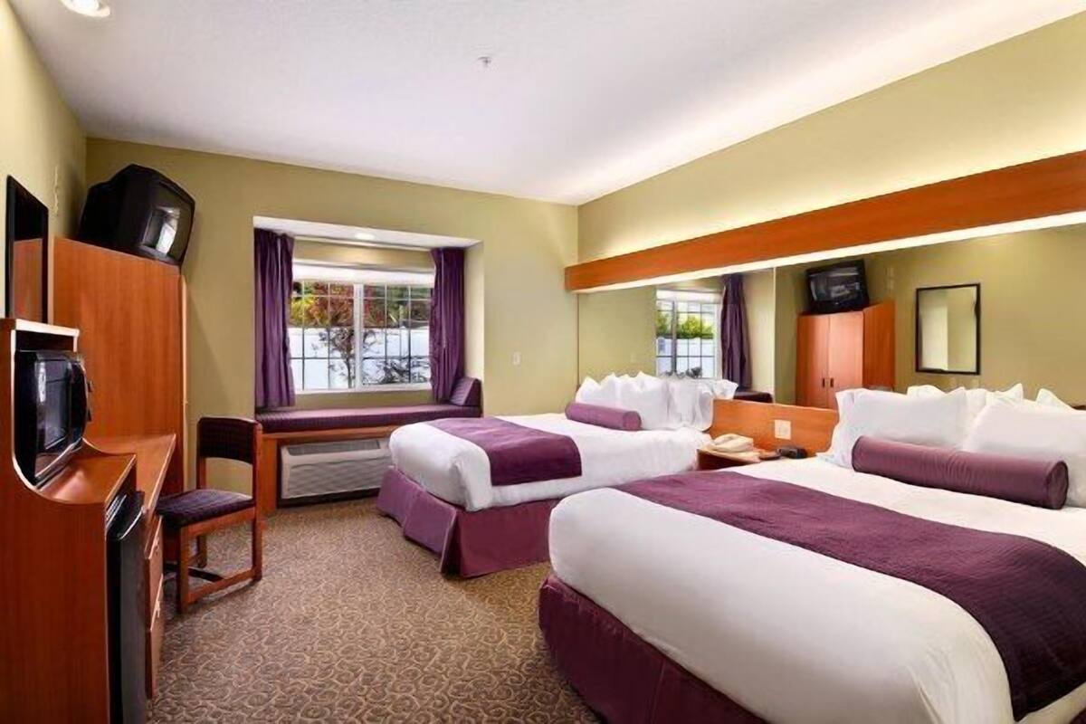Ett hotellrum med två sängar, ett skrivbord, en tv och ett fönster med gardiner.