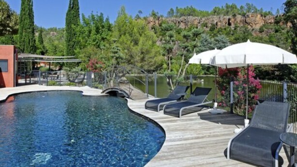 A swimming pool with lounge chairs and umbrellas, surrounded by greenery and a rocky cliff. - Hostellerie Les Gorges de Pennafort (Callas)