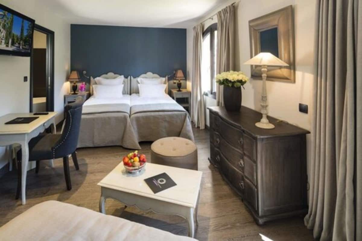 Habitación de hotel con cama doble, escritorio, silla, cómoda y mesita con frutero.