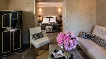 Une chambre d’hôtel comprenant un lit, un canapé, une chaise, une petite table avec un magazine et un arrangement floral décoratif.