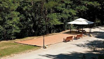 A picnic area with a table and benches under a canopy, surrounded by trees.